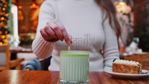 Video - Close up of a woman mixing a matcha latte with a paper straw at a cafe