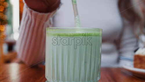 Video - Close up of a woman mixing a matcha latte with a paper straw at a cafe