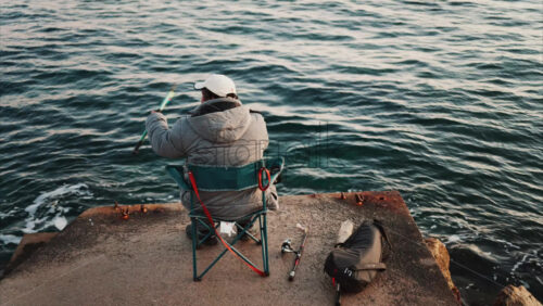 Video - Man in winter clothes on a chair fishing in the sea in the south of France