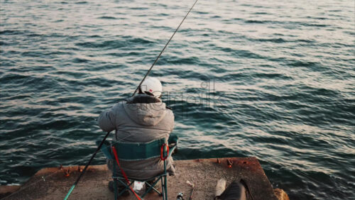 Video - Man in winter clothes on a chair fishing in the sea in the south of France