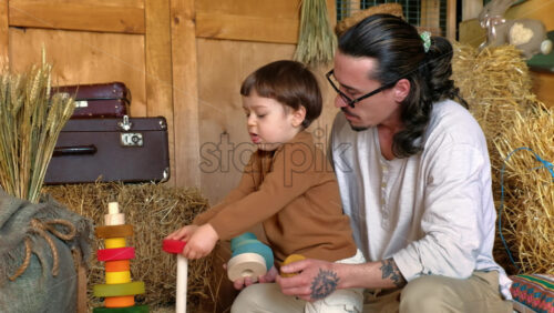 Video - Man playing with child with colourful wooden toys in a barn, near square hay bales