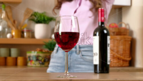 Video - A glass and a bottle of red wine standing on the table in front of a woman dancing in the kitchen
