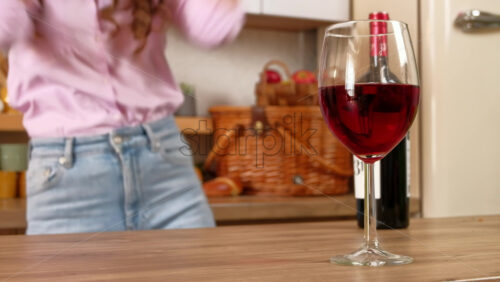 Video - A glass and a bottle of red wine standing on the table in front of a woman dancing in the kitchen