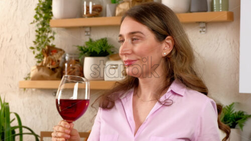 Video - Woman savouring a glass of red wine in the kitchen, in daylight