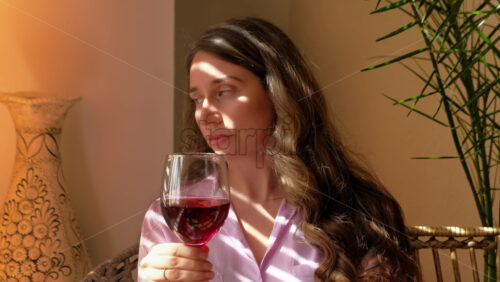 Video - Close up of woman savouring a glass of red wine in the kitchen, in daylight