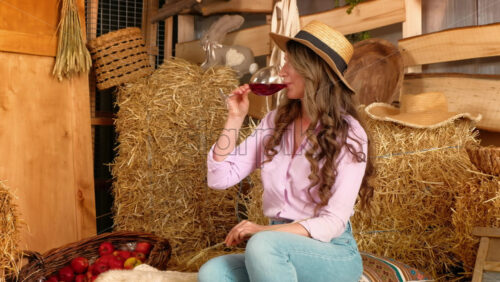 Video - Woman enjoying a glass of red wine in the barn near square hay bales, in daylight