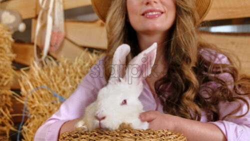 Video - Woman petting a white bunny in the barn near square hay bales, in daylight