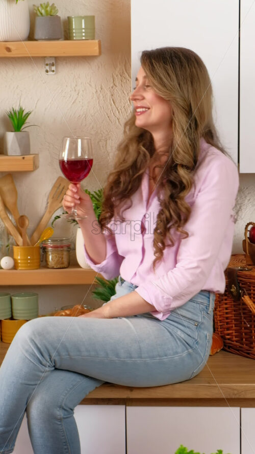 Video - Woman drinking a glass of red wine and dancing in the kitchen. Verical