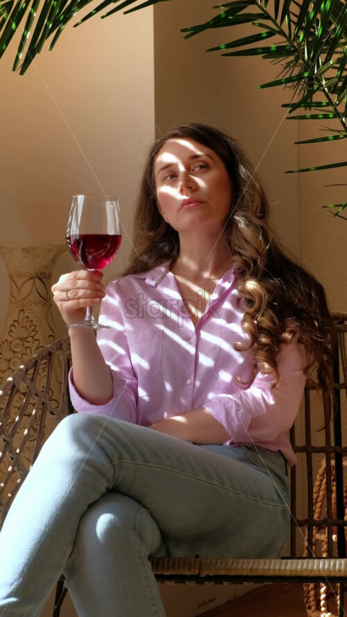 Video - Woman savouring a glass of red wine in daylight. Vertical