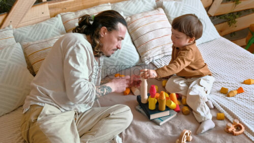 Video - Man playing with child with colourful wooden toys on the bed