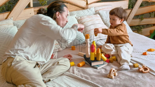Video - Man playing with child with colourful wooden toys on the bed