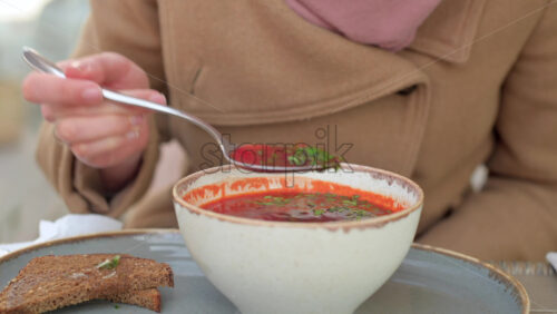 Video - Woman in brown coat eating borscht at a terrace