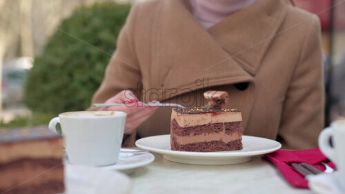 Video - Woman in brown coat eating chocolate cake with coffee at a terrace