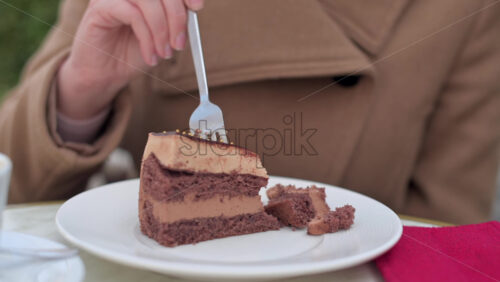 Video - Woman in brown coat eating chocolate cake with coffee at a terrace