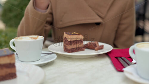 Video - Woman in brown coat eating chocolate cake with coffee at a terrace