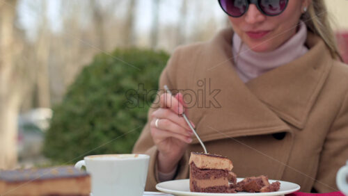 Video - Woman in brown coat eating chocolate cake with coffee at a terrace