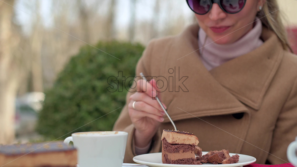 Video - Woman in brown coat eating chocolate cake with coffee at a terrace
