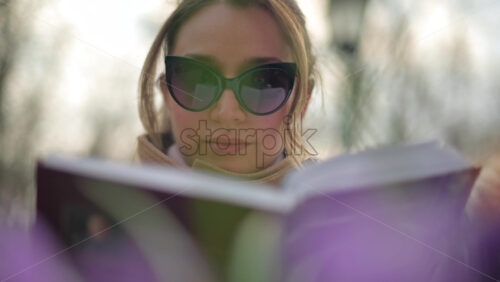 Video - Brunette woman in brown coat reading a book at a terrace