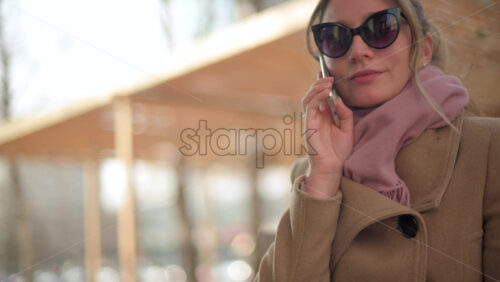 Video - Brunette woman wearing a brown coat talking on the phone at a terrace