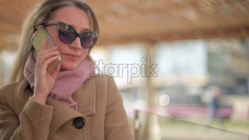 Video - Brunette woman wearing a brown coat talking on the phone at a terrace