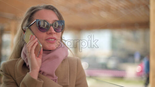 Video - Brunette woman wearing a brown coat talking on the phone at a terrace