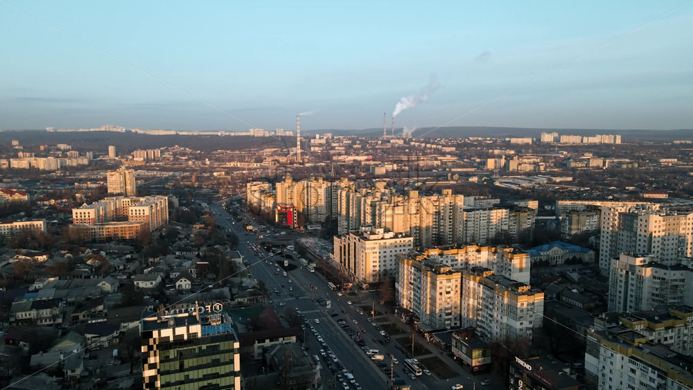 Video - CHISINAU, MOLDOVA - JANUARY 17, 2021: Aerial drone view of city at sunset. Multiple buildings, roads with multiple cars, thermal station's tubes. Bare trees, winter