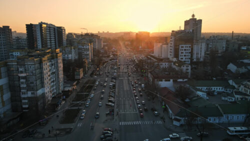 Video - CHISINAU, MOLDOVA - JANUARY 17, 2021: Aerial drone view of city at sunset. Multiple residential and commercial buildings, roads with multiple cars, walking people. Bare trees, winter