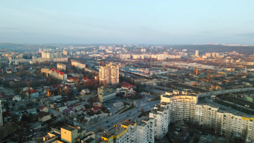Video - Aerial drone view of Chisinau at sunset. Multiple residential buildings, road with cars, bridge over the railroad. Bare trees, winter