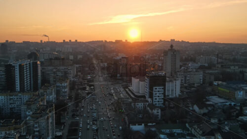 Video - CHISINAU, MOLDOVA - JANUARY 17, 2021: Aerial drone view of city at sunset. Multiple residential and commercial buildings, roads with multiple cars, walking people. Bare trees, winter