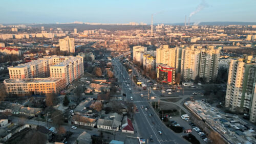 Video - CHISINAU, MOLDOVA - JANUARY 17, 2021: Aerial drone view of city at sunset. Multiple residential buildings, roads with multiple cars, thermal station's tubes. Bare trees, winter