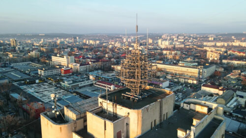 Video - CHISINAU, MOLDOVA - JANUARY 17, 2021: Aerial drone view of an high office building's roof, road with multiple cars, cityscape on the background. Bare trees, winter