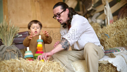 Video - Father playing with his son with colourful, ecological wooden toys in a barn, near square hay bales