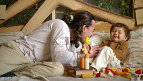 Video - Father playing with his son with colourful, ecological wooden toys on the bed