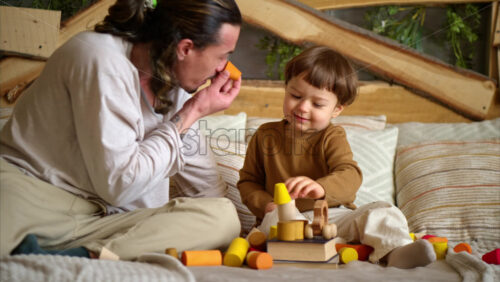Video - Father playing with his son with colourful, ecological wooden toys on the bed