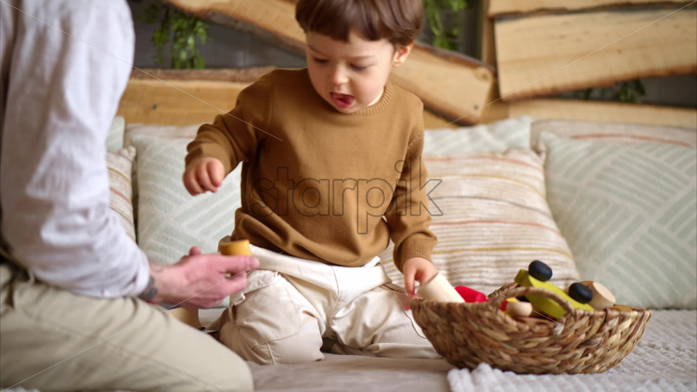 Video - Father playing with his son with colourful, ecological wooden toys on the bed