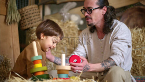 Video - Father playing with his son with colourful, ecological wooden toys in a barn, near square hay bales