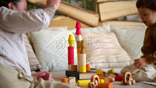 Video - Father playing with his son with colourful, ecological wooden toys on the bed
