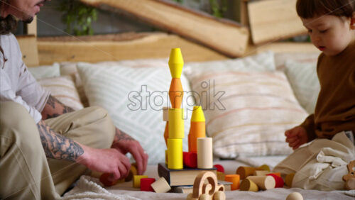 Video - Father playing with his son with colourful, ecological wooden toys on the bed