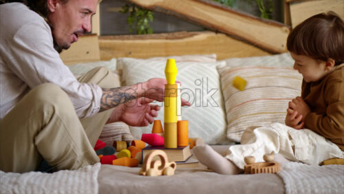 Video - Father playing with his son with colourful, ecological wooden toys on the bed