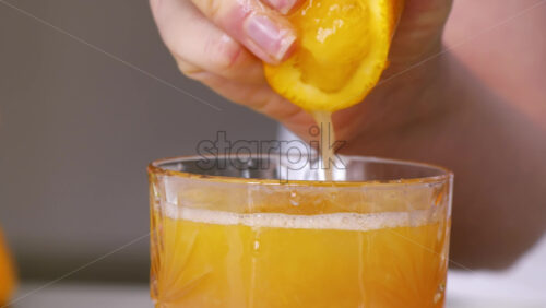Video - A woman squeezes juice from an orange into a glass. Slow motion