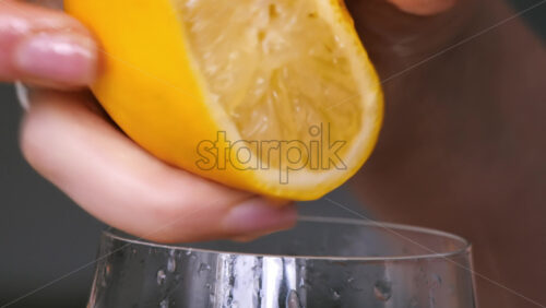 Video - A woman squeezes juice from a lemon into a glass. Slow motion