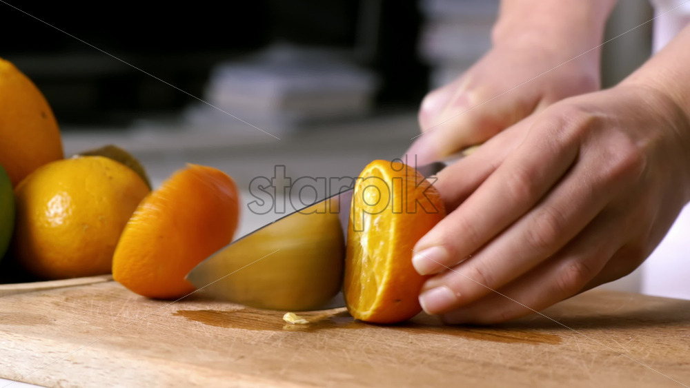 Video - Woman slicing orange in two parts on a wooden board. Fruits on the background. Slow motion