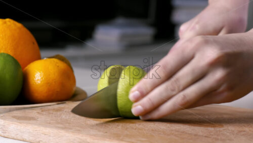 Video - Woman slicing lime in two parts on a wooden board. Fruits on the background. Slow motion