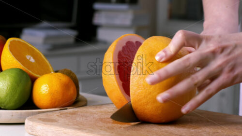 Video - Woman slicing grapefruit in two parts on a wooden board. Fruits on the background. Slow motion