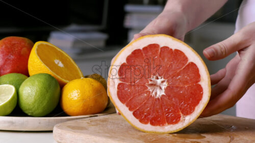Video - Woman showing cutted part of a grapefruit on a wooden board. Fruits on the background. Slow motion
