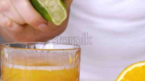 Video - A woman squeezes juice from a lime into a glass. Slow motion