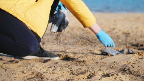 Video - Man in medical gloves picking up a bunch of dirty medical masks from the beach of a lake. Pollution idea