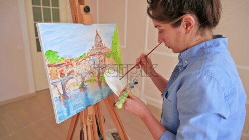 Video - Woman mixing paints on a palette and painting picture on the easel at home. Slow motion