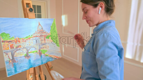 Video - Caucasian woman painting a picture with a palette in her hands and listening music with earphones indoors