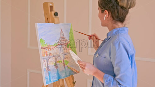 Video - Caucasian woman painting a picture with a palette in her hands and listening music with earphones indoors. Slow motion